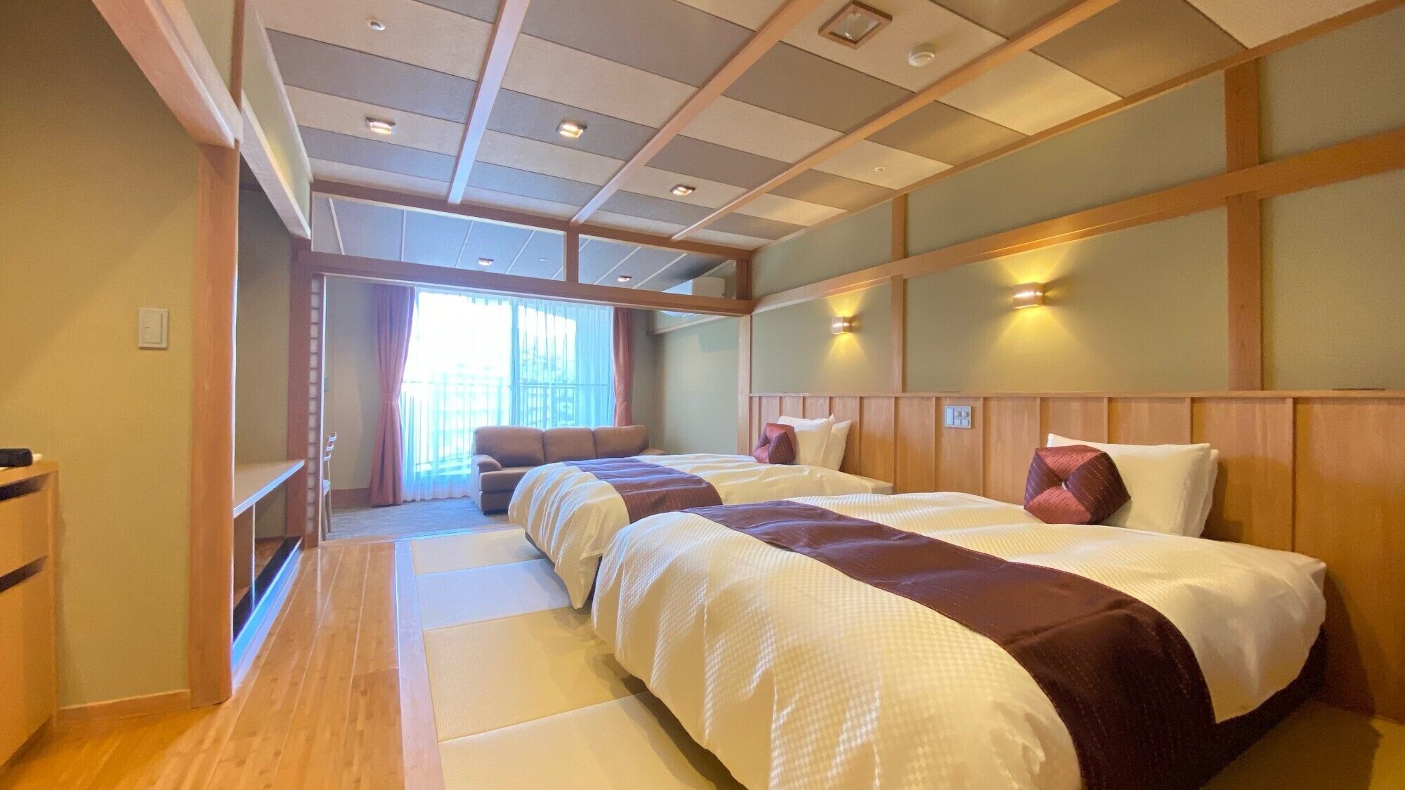 Habitación de hotel con una cama grande, un sofá, suelo de madera y vistas al exterior.