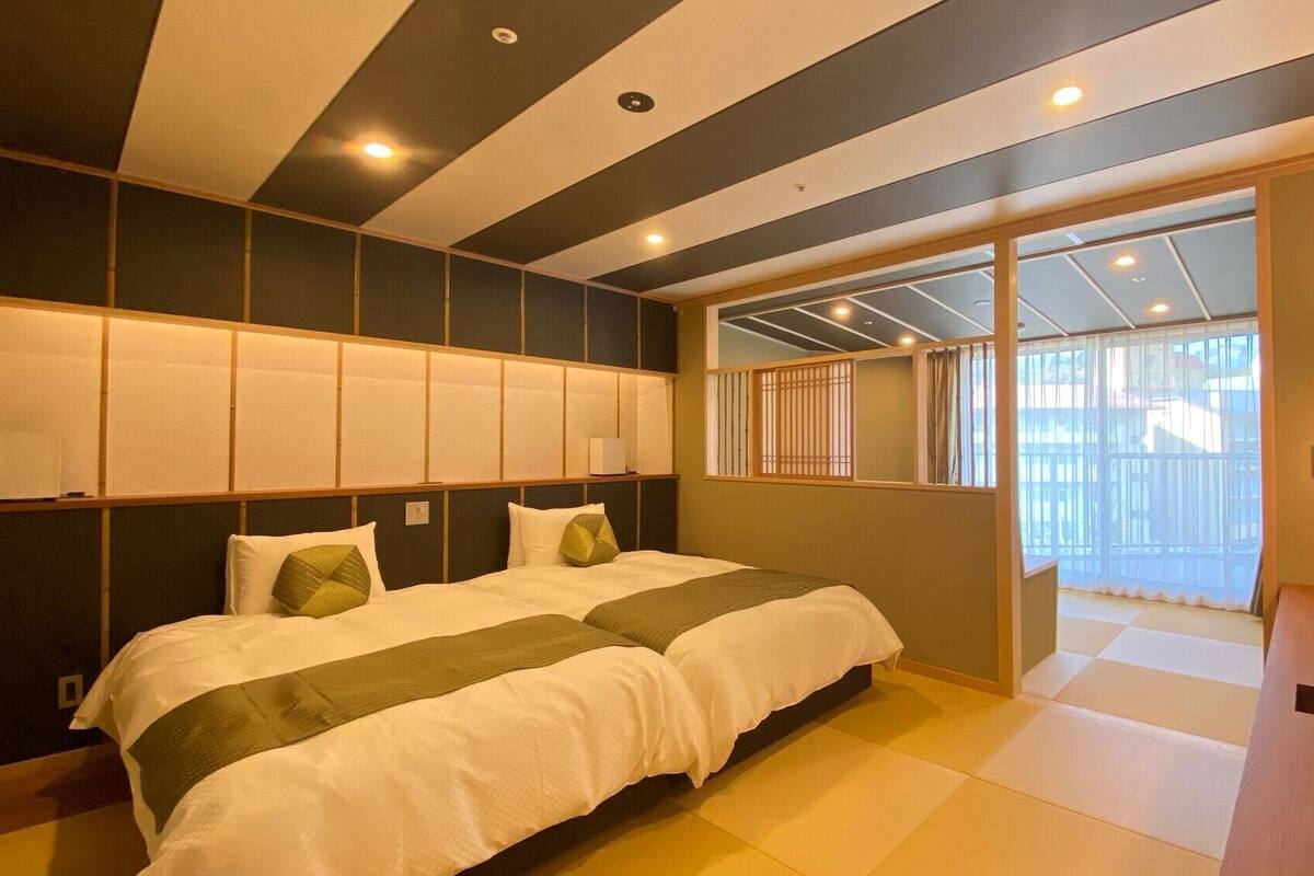 A hotel room with a bed, a desk with a phone, and a view through a window.