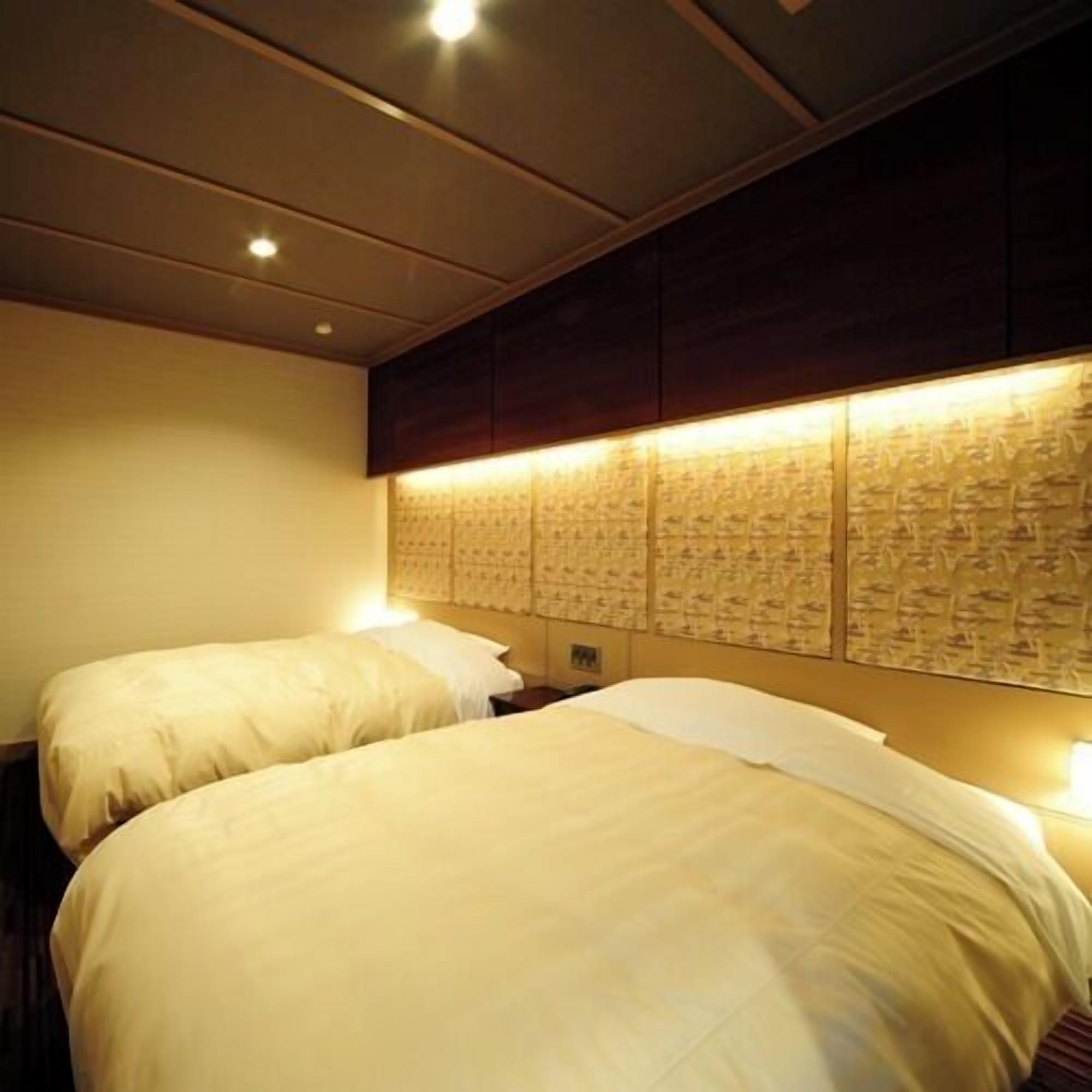 A hotel room with two beds, a headboard with a patterned design, and recessed ceiling lighting.