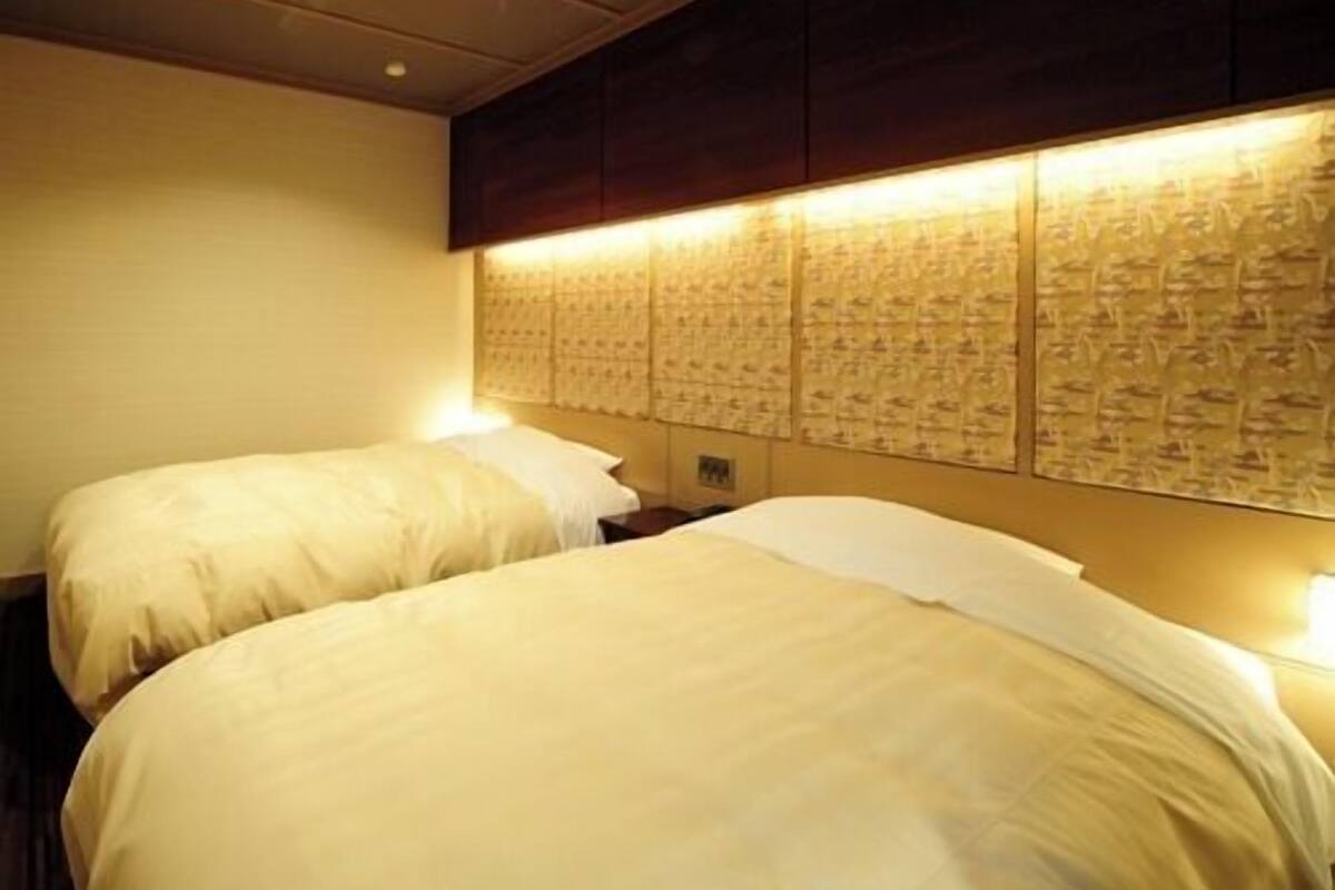 A hotel room with two beds, a headboard with a patterned design, and recessed ceiling lighting.