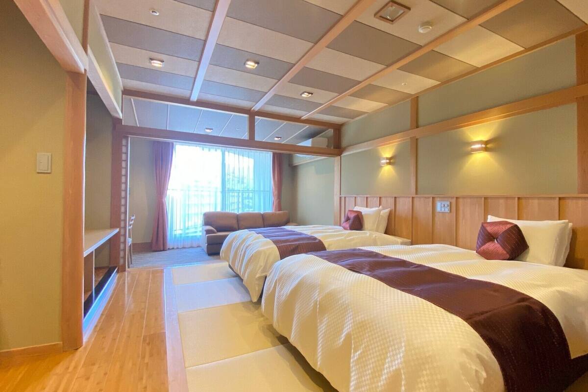 A hotel room with a large bed, a sofa, a wooden floor, and a view of the outside.