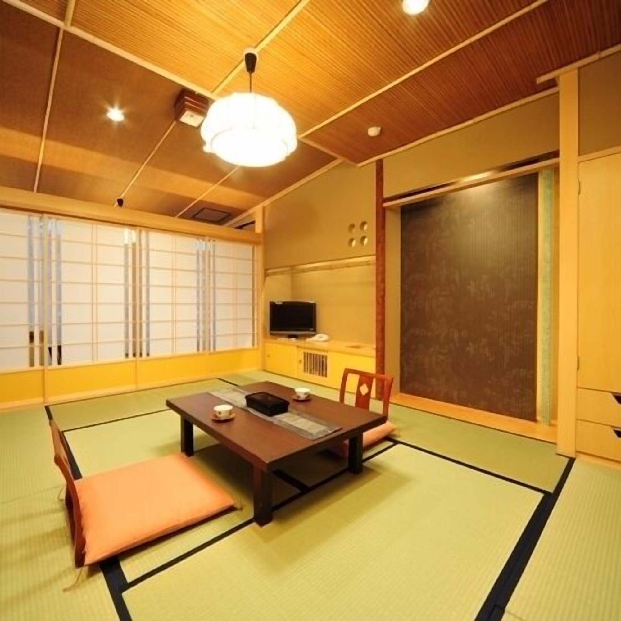 Una habitación japonesa tradicional con suelo de tatami, una mesa baja con cojines, un televisor y puertas correderas.