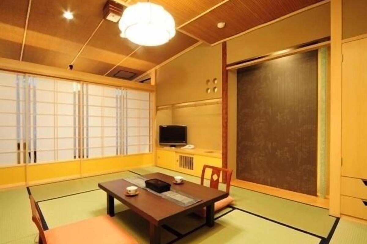 A traditional Japanese room with tatami flooring, a low table with cushions, a television, and sliding doors.