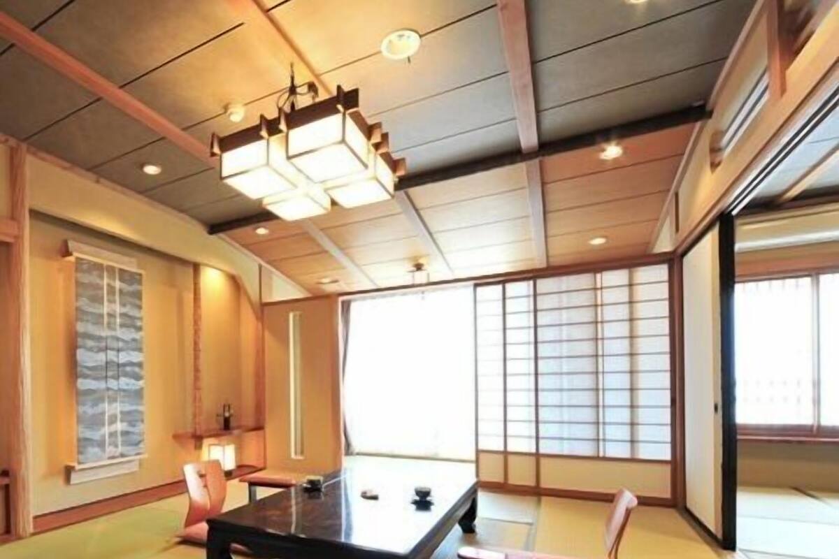 A tatami mat room with a low table, cushions, sliding doors, and a ceiling light fixture.