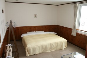 A bedroom with a wooden paneled wall, a bed with white bedding, a window with a curtain, and a towel rack. - Pension ASHITAYA (Furano)