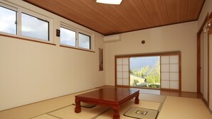 A tatami mat room with a wooden table, sliding doors, and a view of greenery outside. - Pension ASHITAYA (Furano)