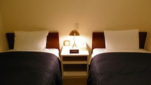 Et hotelværelse med to senge, hver med sengegavl, et natbord med lampe og et lille kort på bordet.