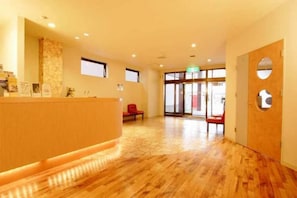 A reception area with a wooden reception desk, a stone accent wall, and a large glass door leading outside. - Horin Hotel (Chitose)