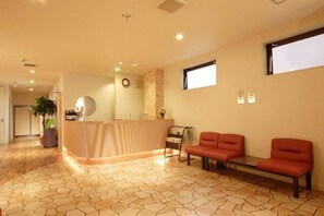 A reception area with a reception desk, two red chairs, a potted plant, and a clock on the wall. - Horin Hotel (Chitose)