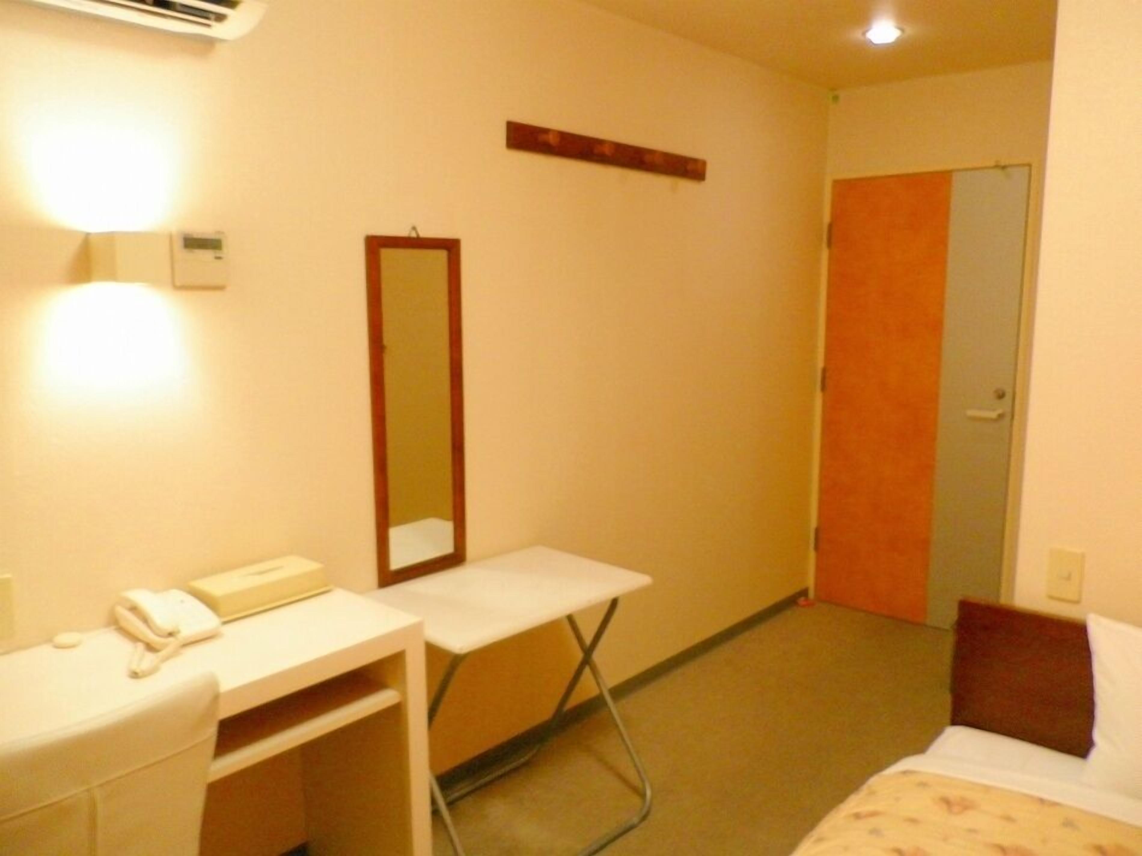 A hotel room with a bed, a desk with a phone, a mirror, and a door.