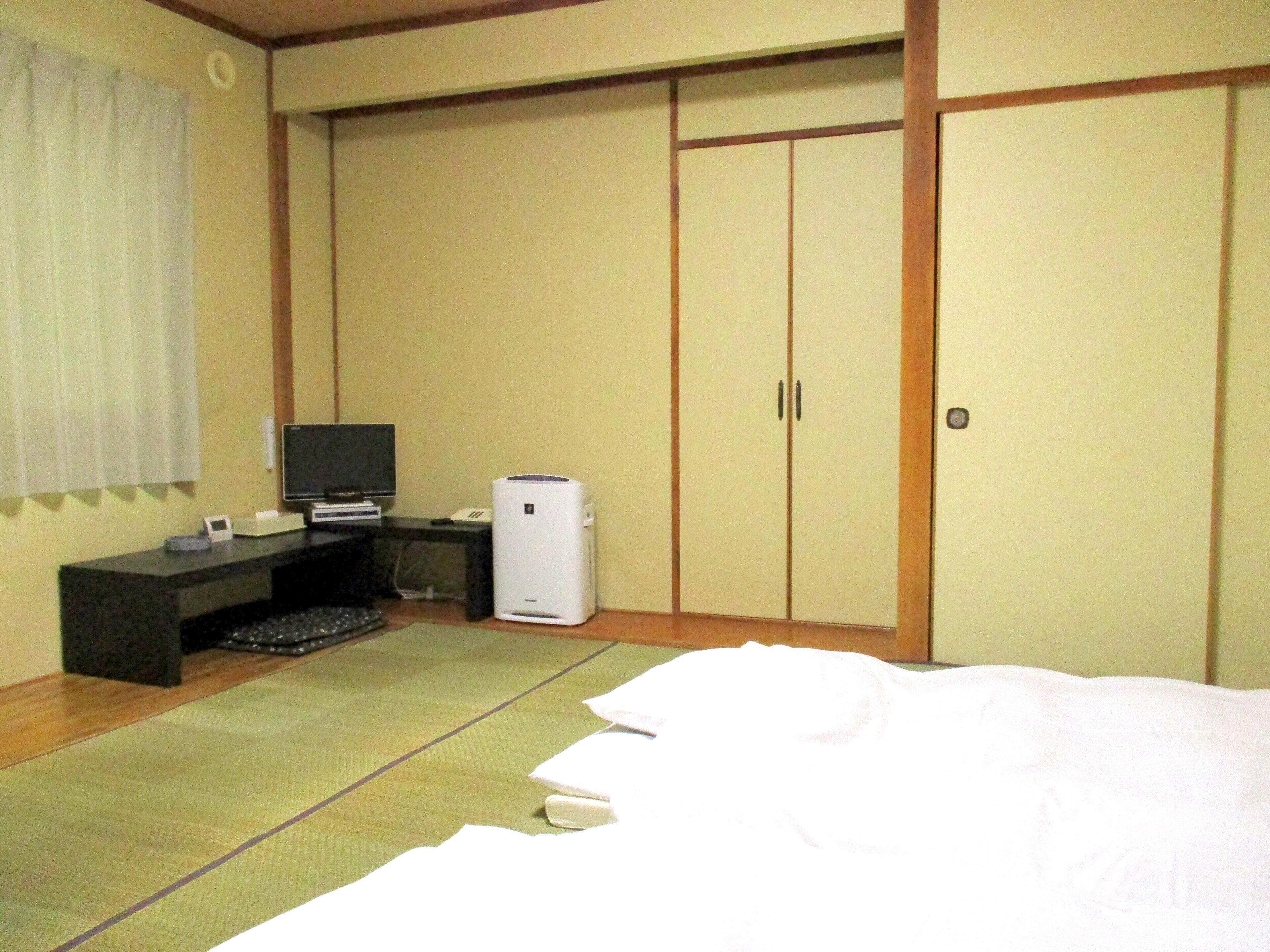 A hotel room with a bed, a desk with a computer, a TV, and a wardrobe.