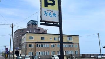 Un immeuble à plusieurs étages, avec un panneau indiquant un parking, une enseigne avec du texte en japonais et plusieurs voitures garées.