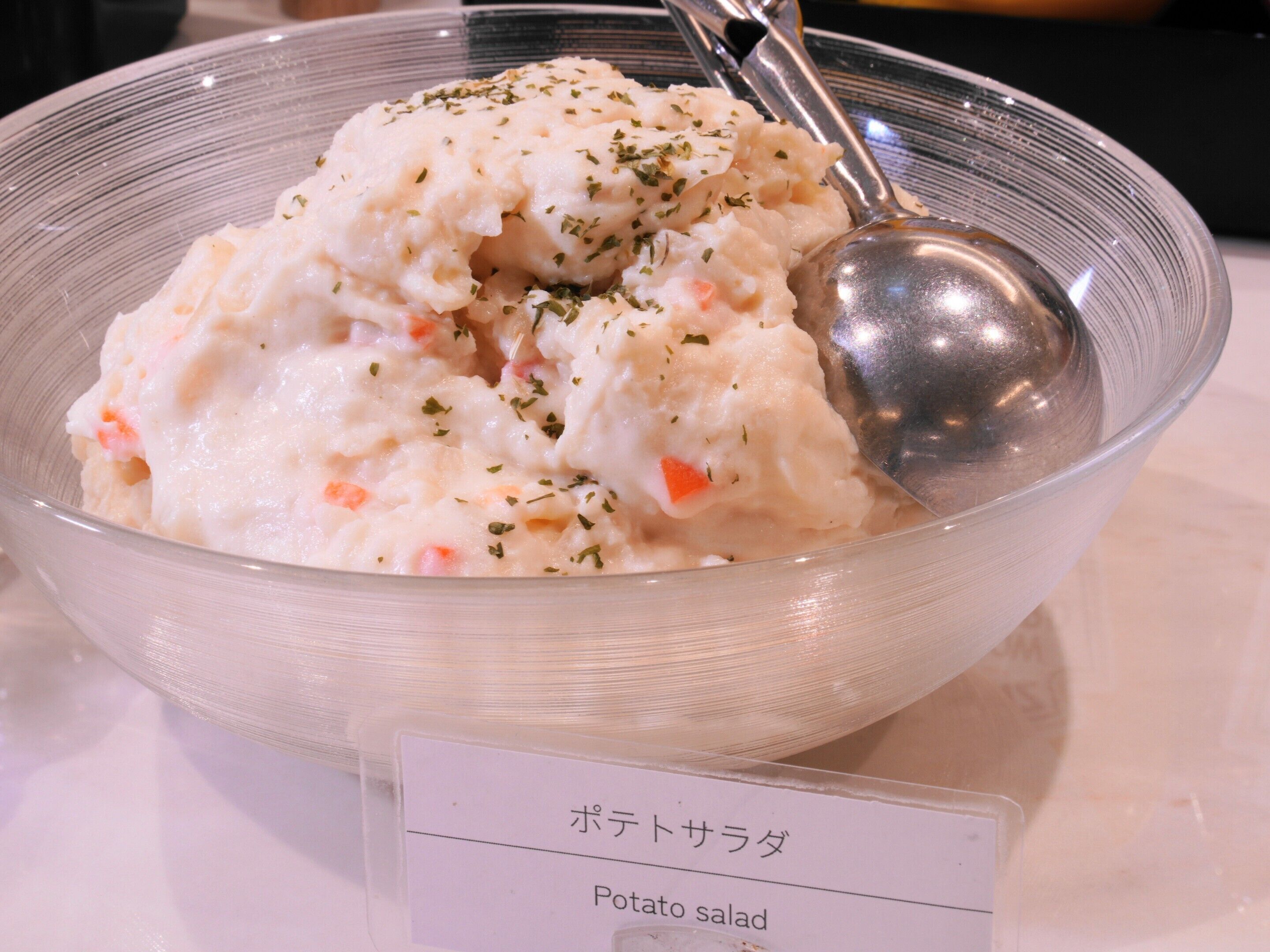 A bowl of potato salad with a spoon, garnished with herbs, and a label indicating it's a potato salad.