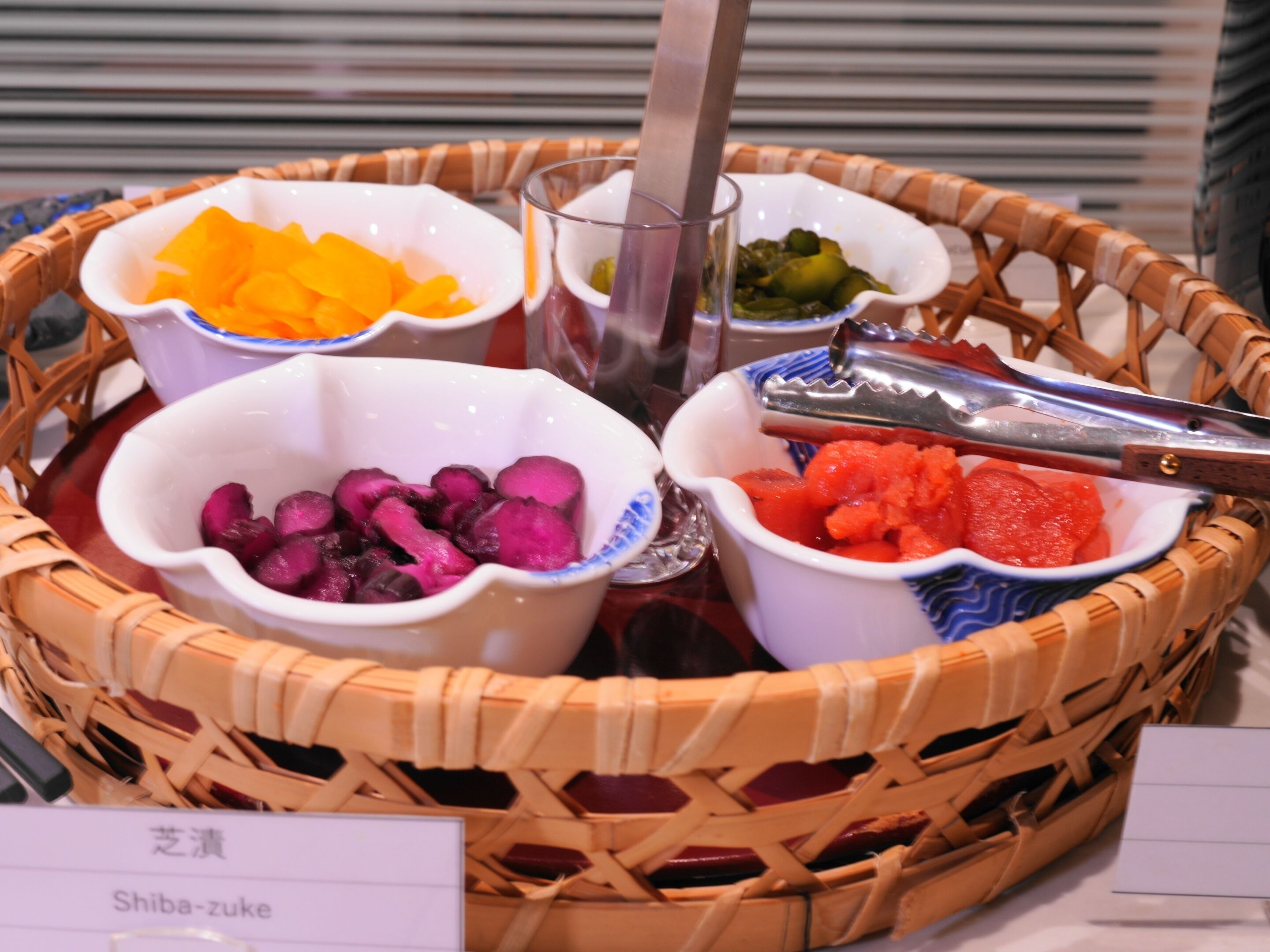 A basket containing various food items, including orange and purple vegetables, and a pair of tongs.