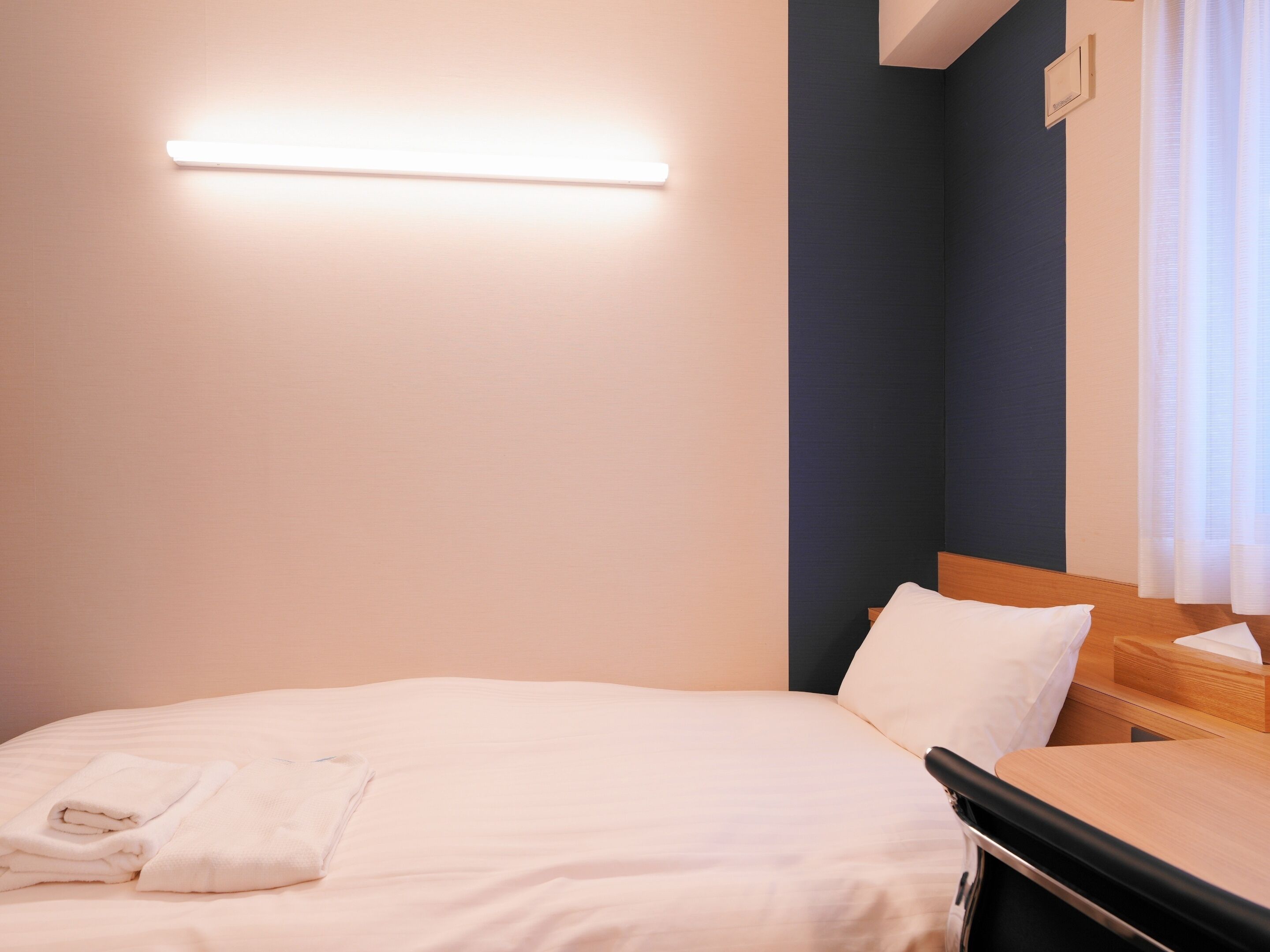 Ein Hotelzimmer mit Bett, Nachttisch, Wandlampe und einem Fenster mit Vorhängen.