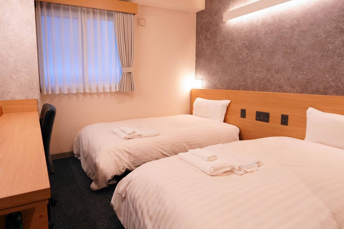 Ein Hotelzimmer mit zwei Betten, einem Schreibtisch und einem Fenster mit Vorhängen.
