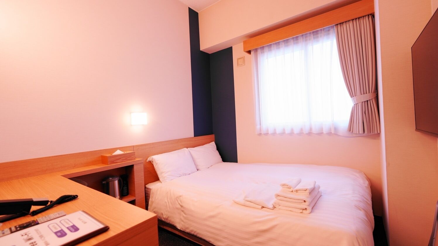 A hotel room with a bed, a desk, a lamp, and a window with curtains.