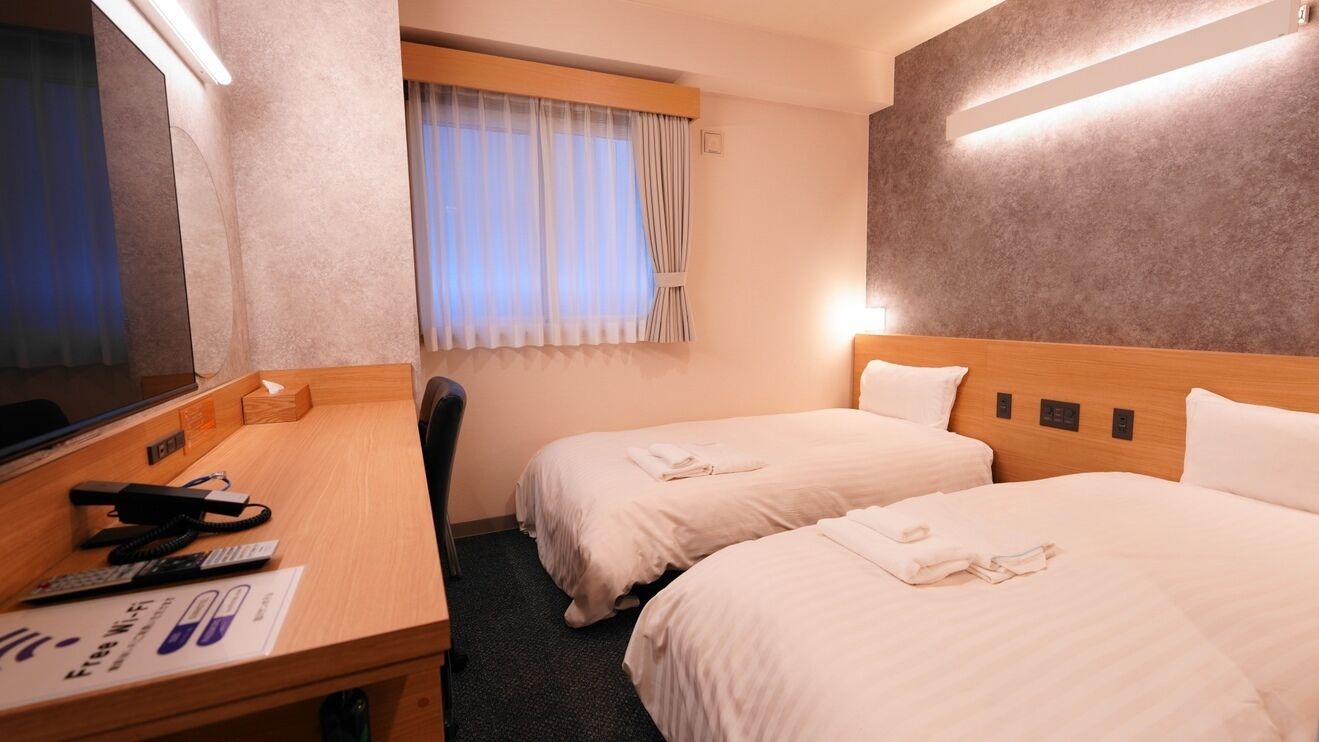 A hotel room with two beds, a desk with a telephone, and a window with curtains.