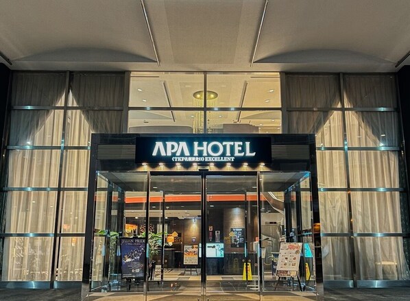 Entrada do APA HOTEL com design moderno, grandes portas de vidro e uma placa indicando ser um estabelecimento 5 estrelas.