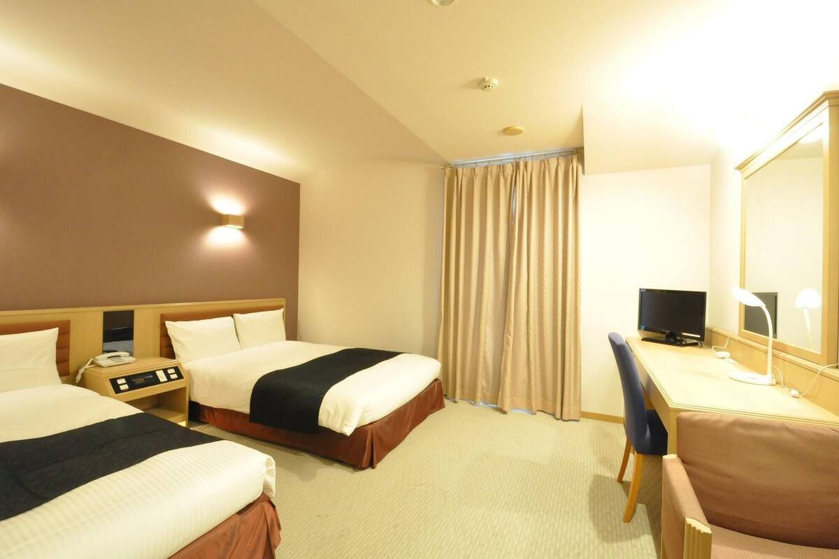 A hotel room with two beds, a desk with a computer, a telephone, and a mirror.