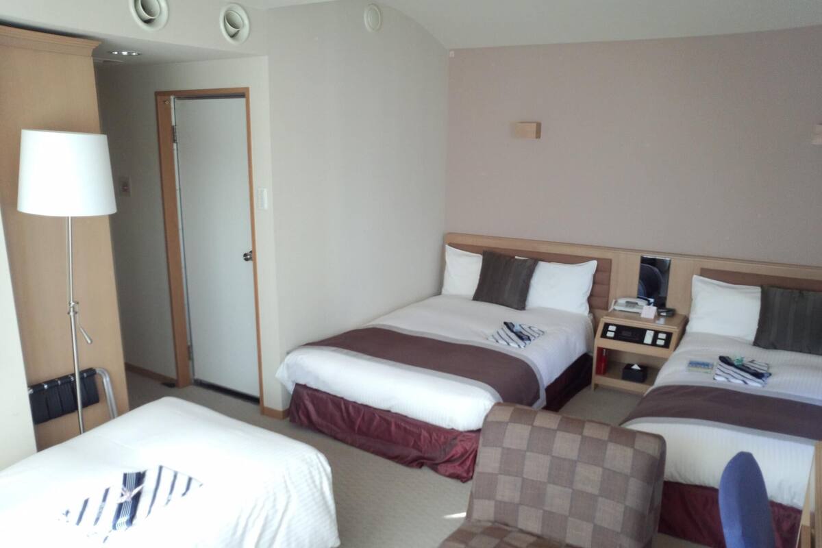 A hotel room with two beds, a desk, a chair, and a lamp.