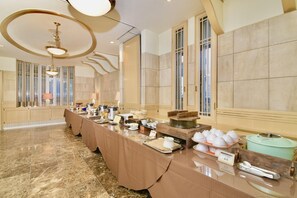 Disposição de buffet em um salão amplo com piso de mármore, grandes janelas e um lustre moderno.
