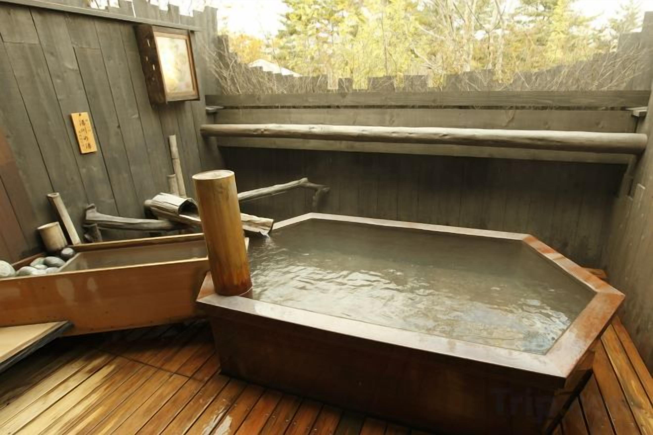 A traditional Japanese onsen with a wooden deck and a stone hot spring.