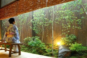 A person seated on a bench in a room with a view of a garden with trees and rocks. - Konoha (Kusatsu)