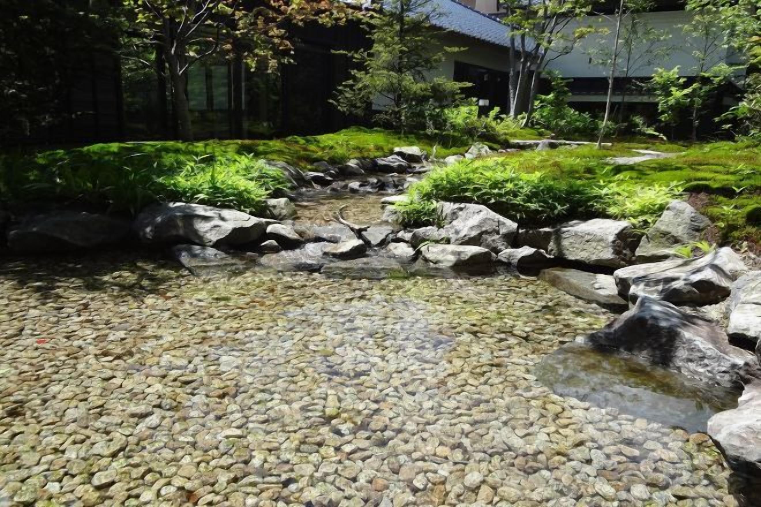 A garden with a stream, rocks, and greenery.