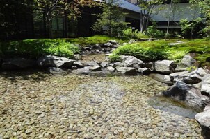 Un jardín con un arroyo, rocas y abundante vegetación.
