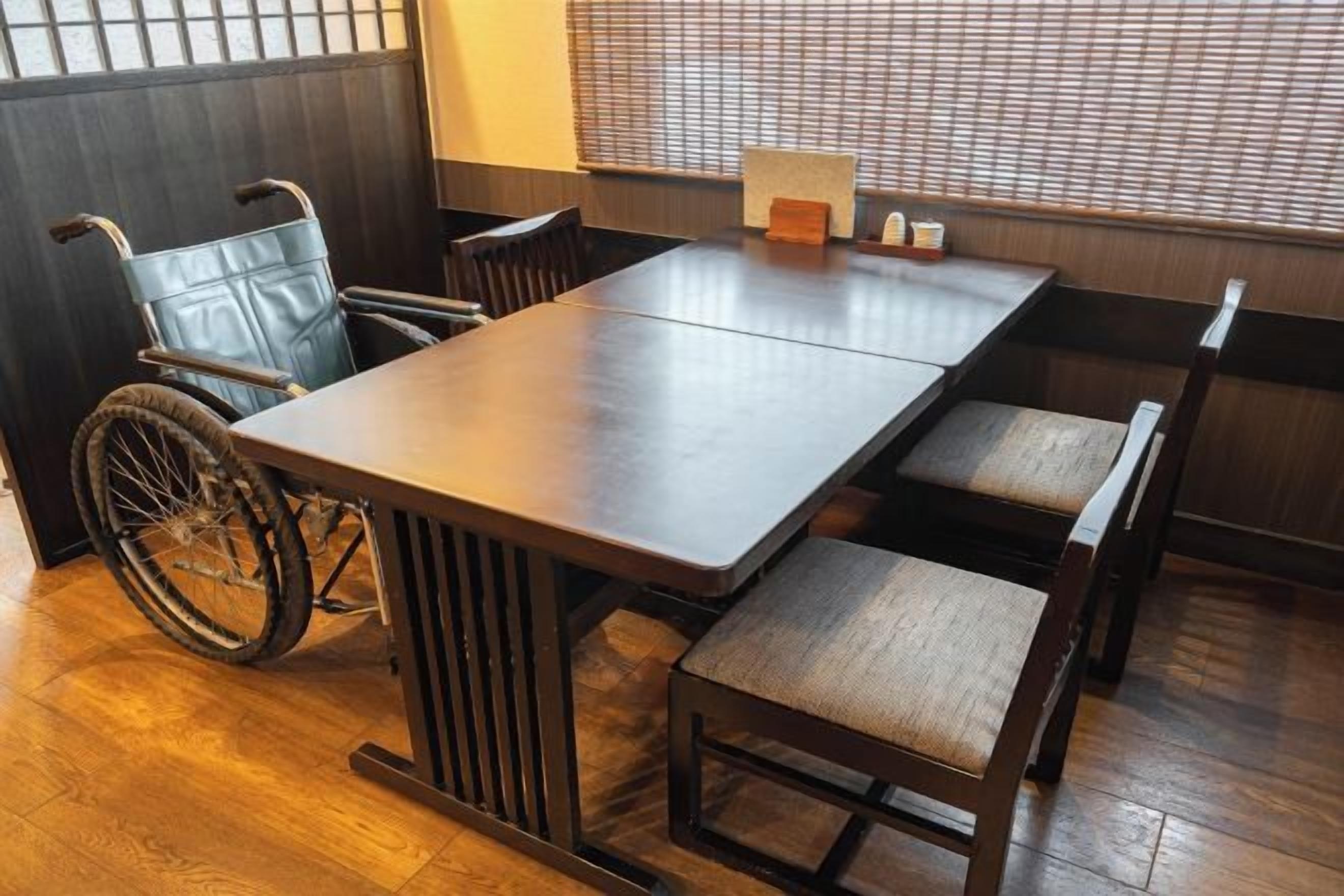 Mesa para comer accesible en silla de ruedas, con sillas, un banco y una ventana con persianas.