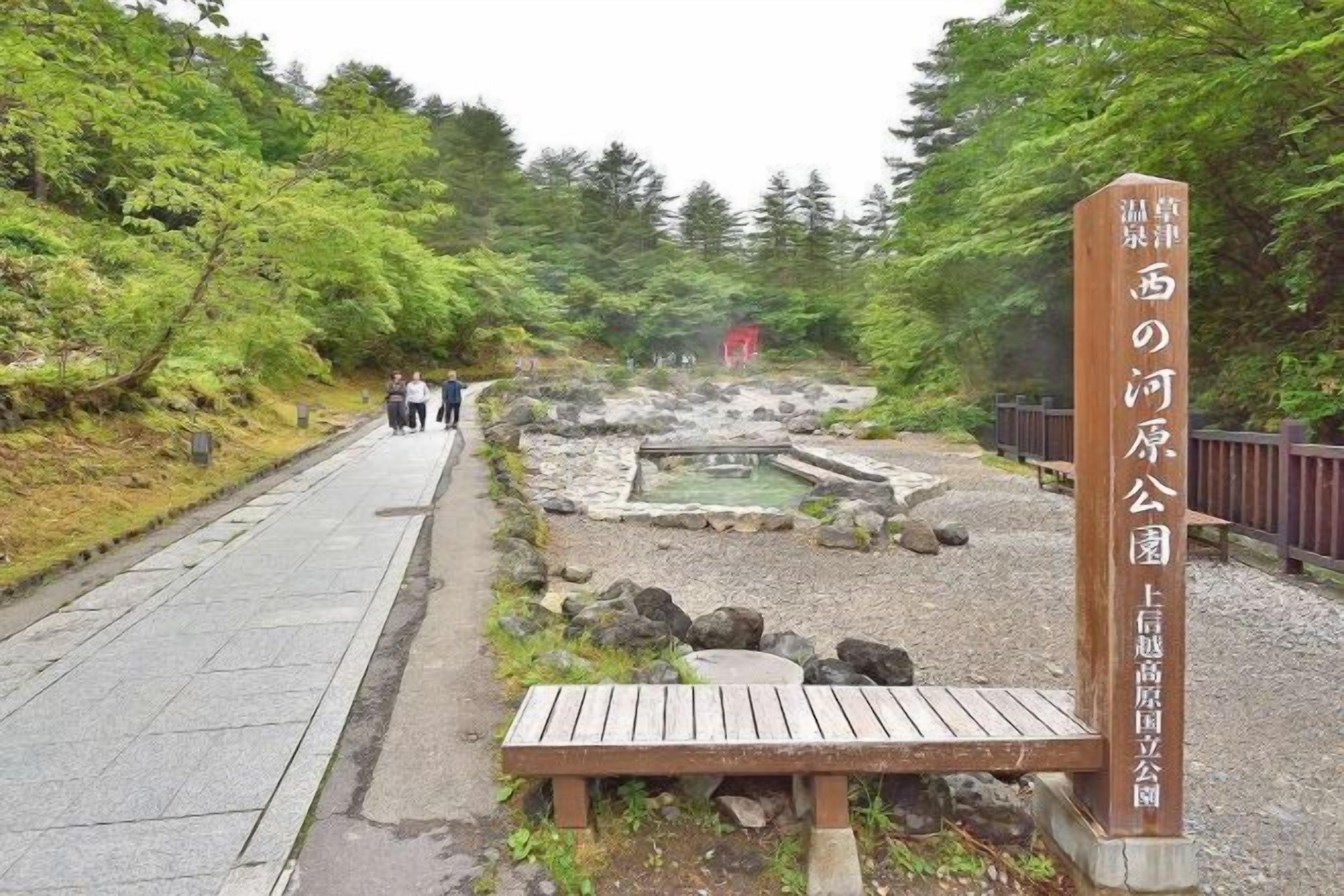 A pathway leading to a natural area with a wooden signpost and a bench.