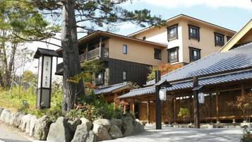 A traditional Japanese building with a stone pathway, wooden structures, and a large tree.