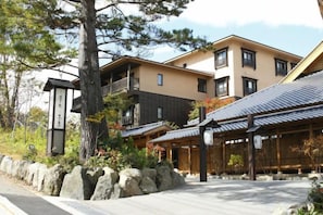 A traditional Japanese building with a stone pathway, wooden structures, and a large tree.