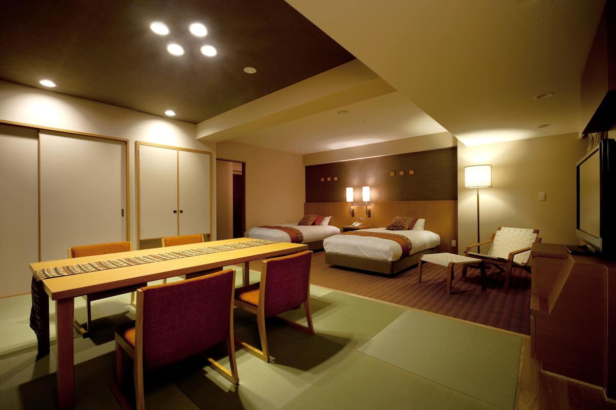 A hotel room with a dining table, two beds, a TV, and a desk.