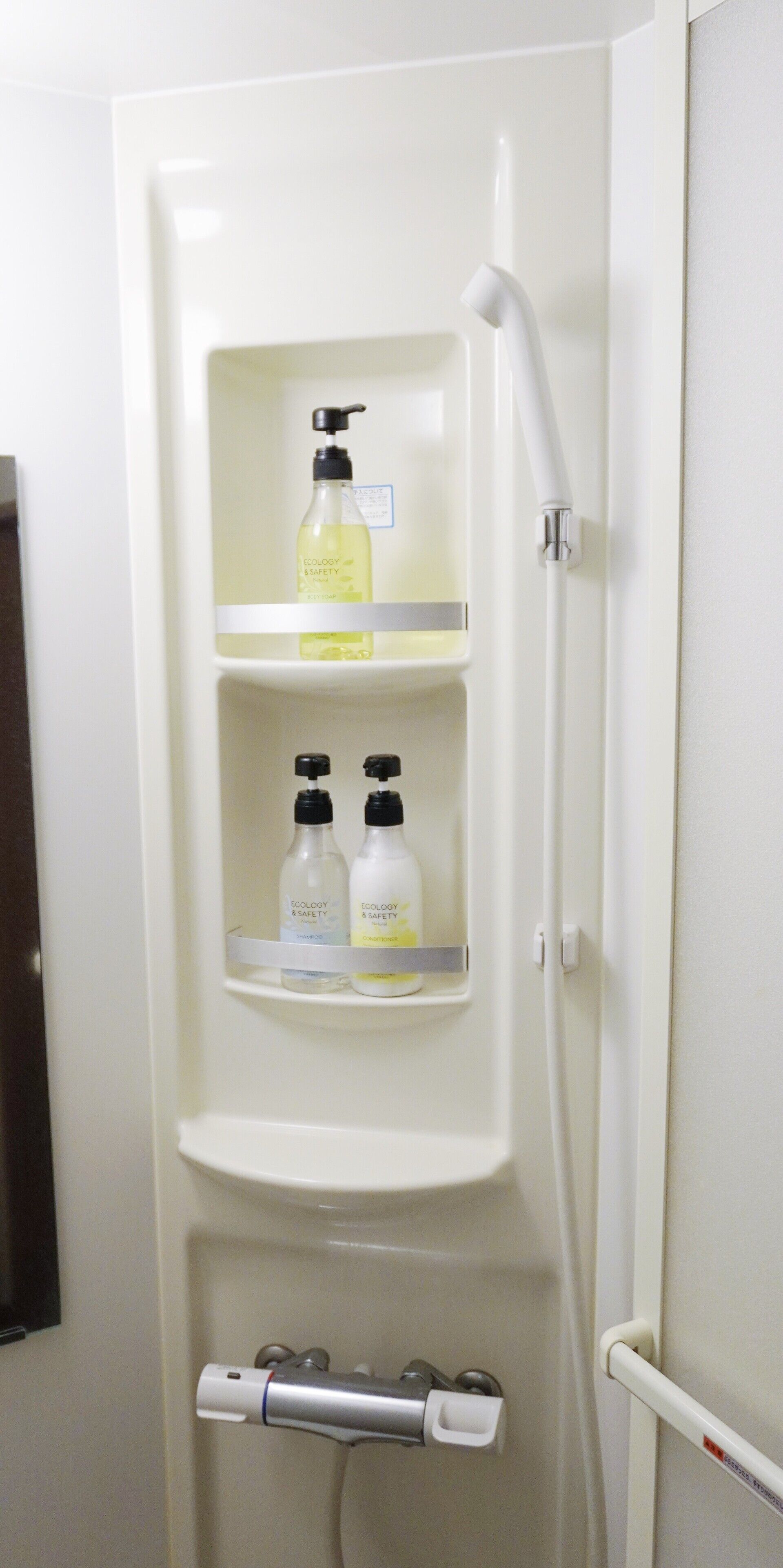A bathroom with a built-in shelf holding toiletries, a showerhead, and a towel rack.