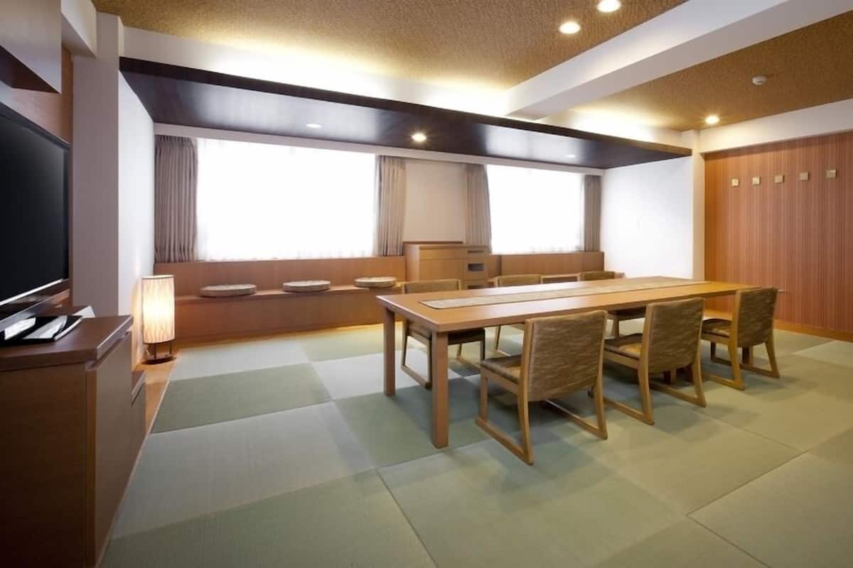 Une pièce avec une table en bois, des chaises, un téléviseur et une fenêtre avec des rideaux.