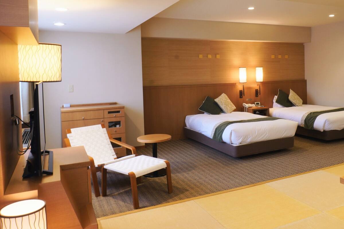 A hotel room with two beds, a desk, a chair, a lamp, and a small table.