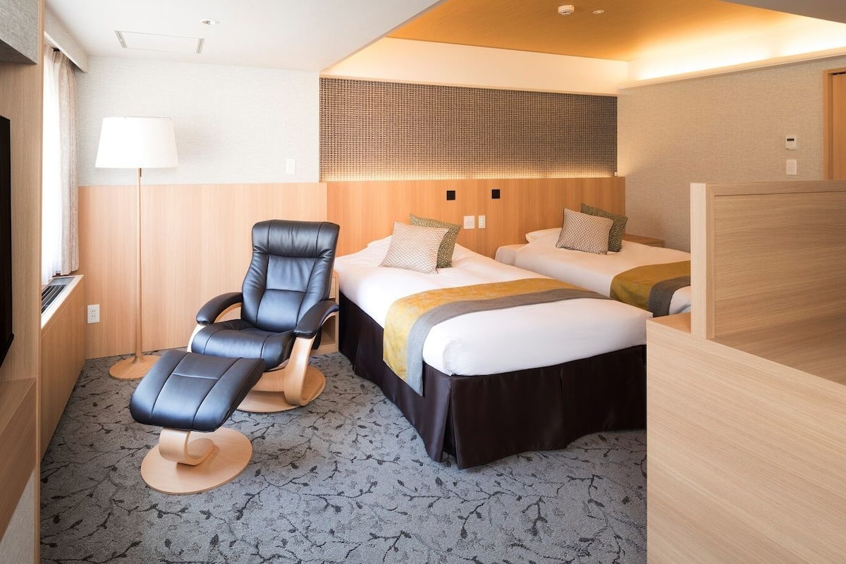 A hotel room with a bed, a massage chair, a desk, and a TV.