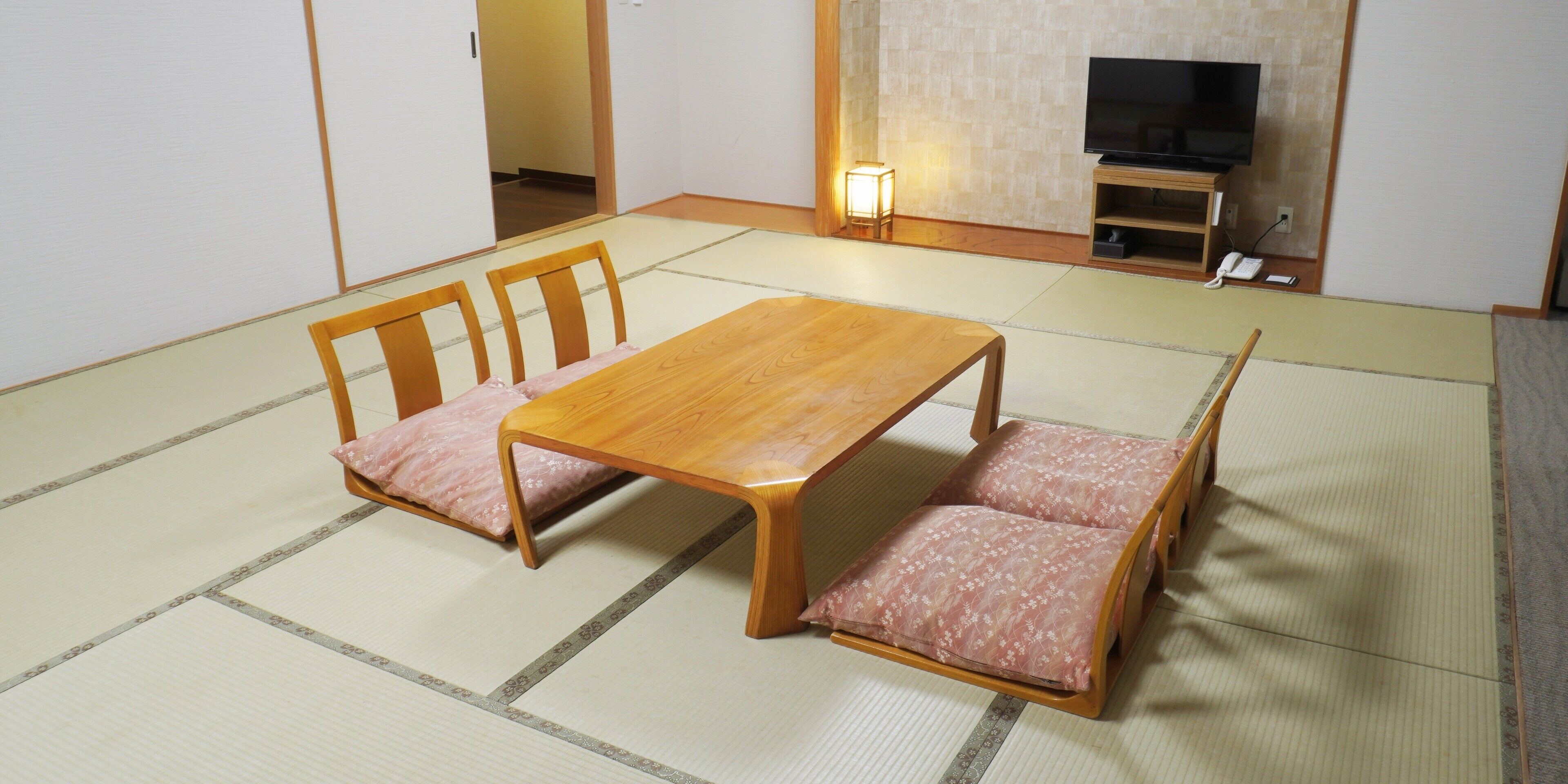 Una habitación con tatami, una mesa de madera y sillas, un televisor y un estante pequeño.
