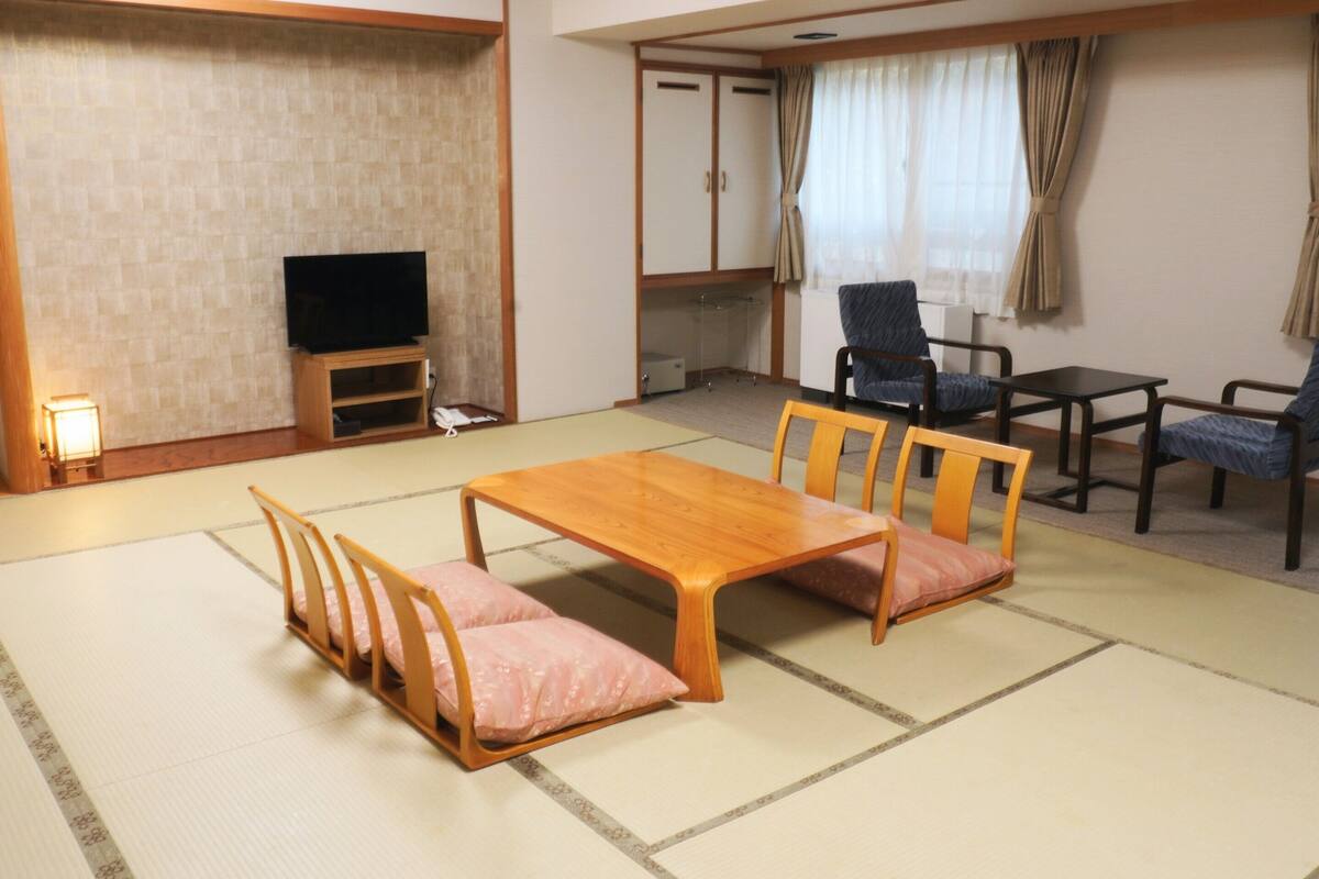 A traditional Japanese-style room with tatami flooring, a low wooden table with cushions, and a television.