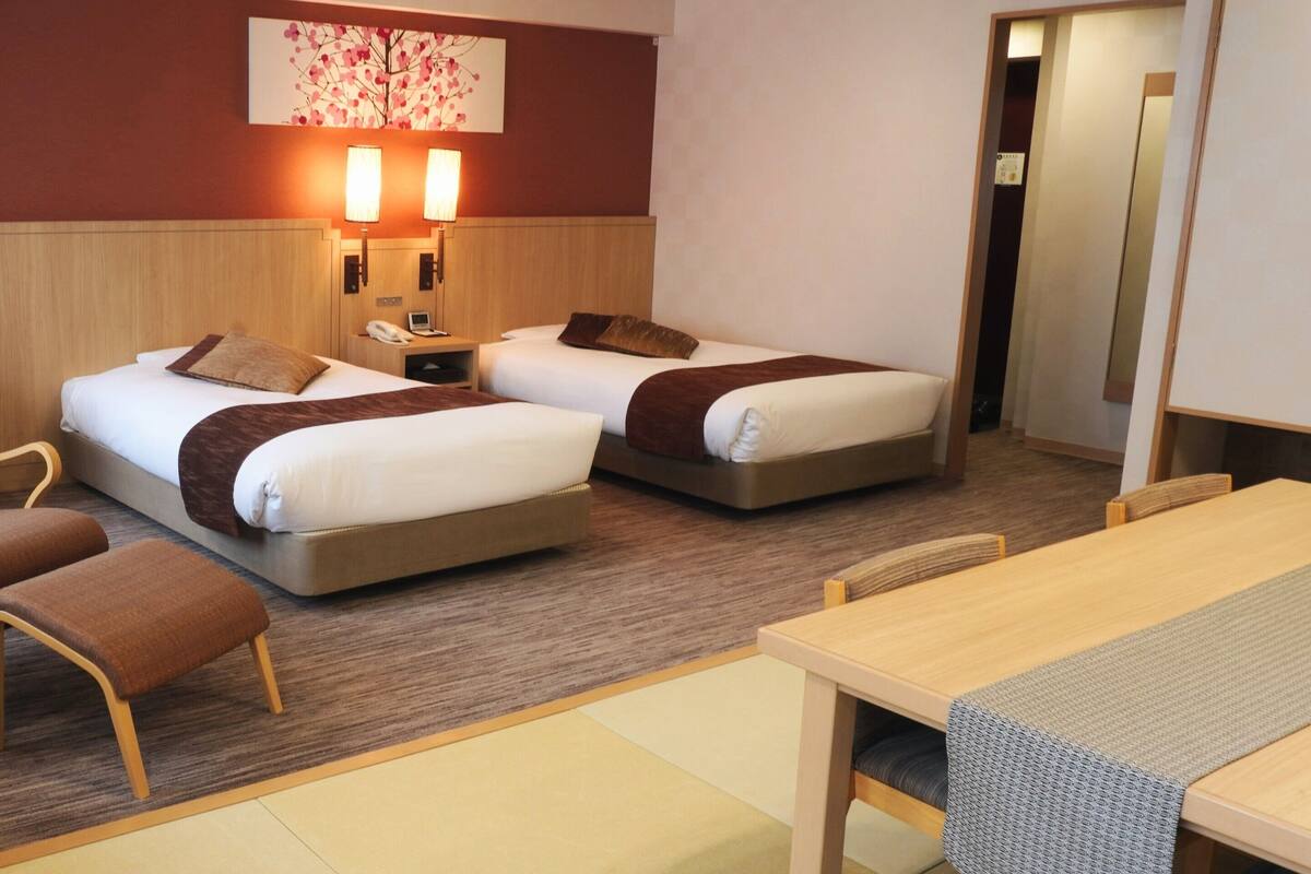 A hotel room with two beds, a desk, a chair, and a television.