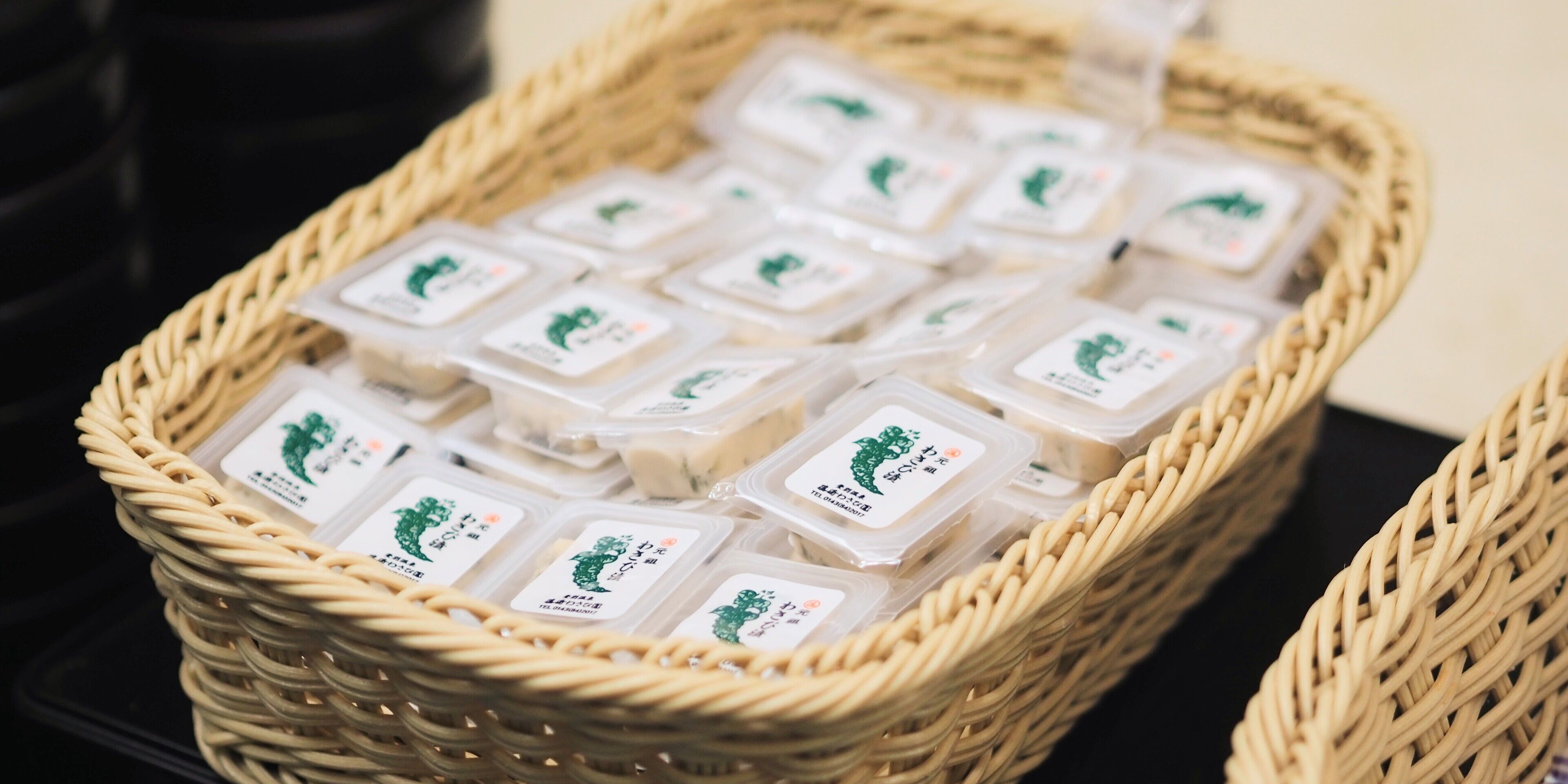 A wicker basket filled with small plastic containers, each with a label featuring a green tree and Japanese characters.