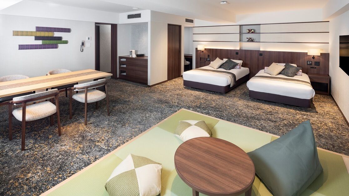 Une chambre d’hôtel avec une table à manger, deux lits, un canapé et une petite table.