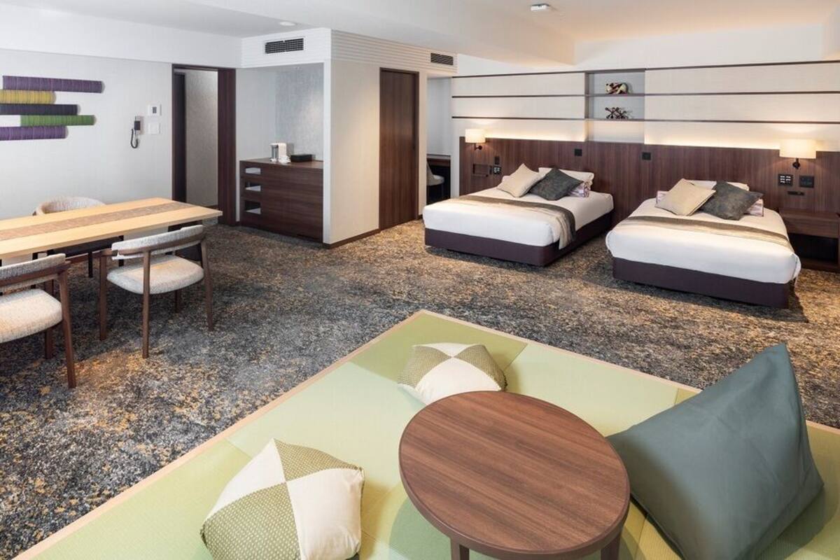 A hotel room with a dining table, two beds, a sofa, and a small table.