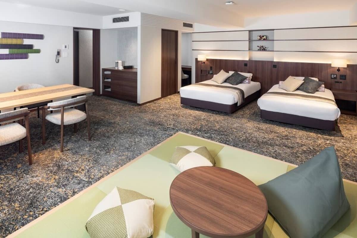 Une chambre d’hôtel avec une table à manger, deux lits, un canapé et une petite table.