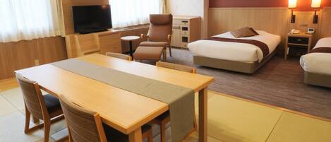A hotel room with a wooden dining table, two beds, a TV, and a desk with a lamp.