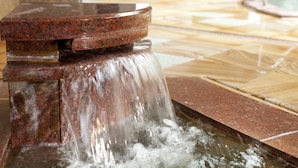 Un élément décoratif aquatique composé d’un bassin circulaire et d’une fontaine, installé dans un espace revêtu de carreaux.