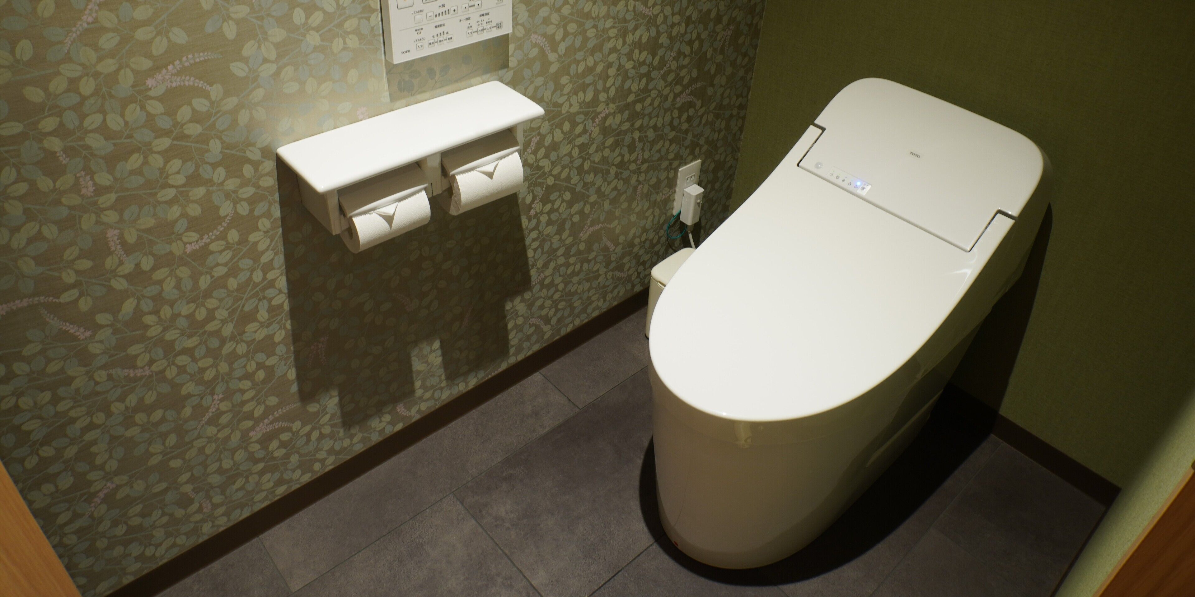Un baño con inodoro, dispensador de toallas de papel y toma de corriente en la pared.