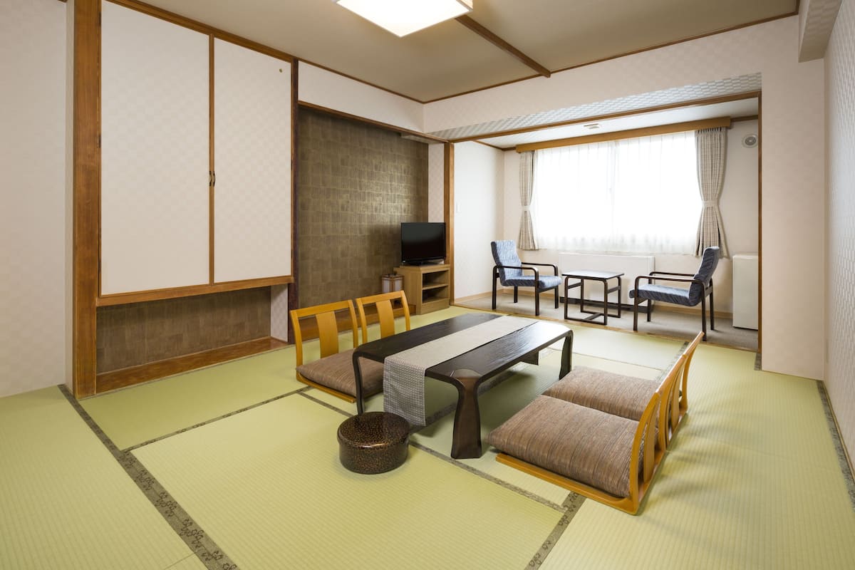 A traditional Japanese room with tatami flooring, a low table, cushions, a television, and sliding doors.